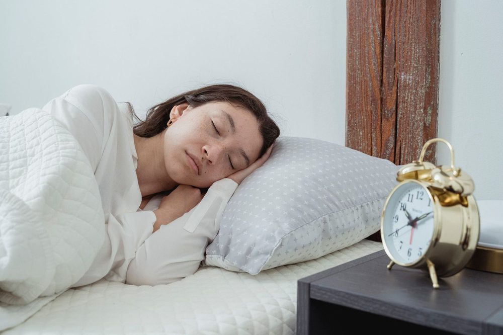 Woman sleeping peacefully in a bright bedroom next to an alarm clock — magnesium for sleep from food and supplements