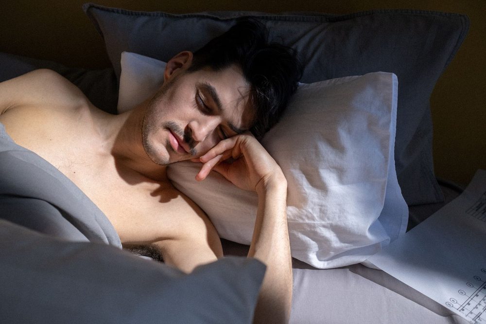 Junger Mann schläft im Bett bei sanftem Morgenlicht – kann man Schlaf nachholen am Wochenende?