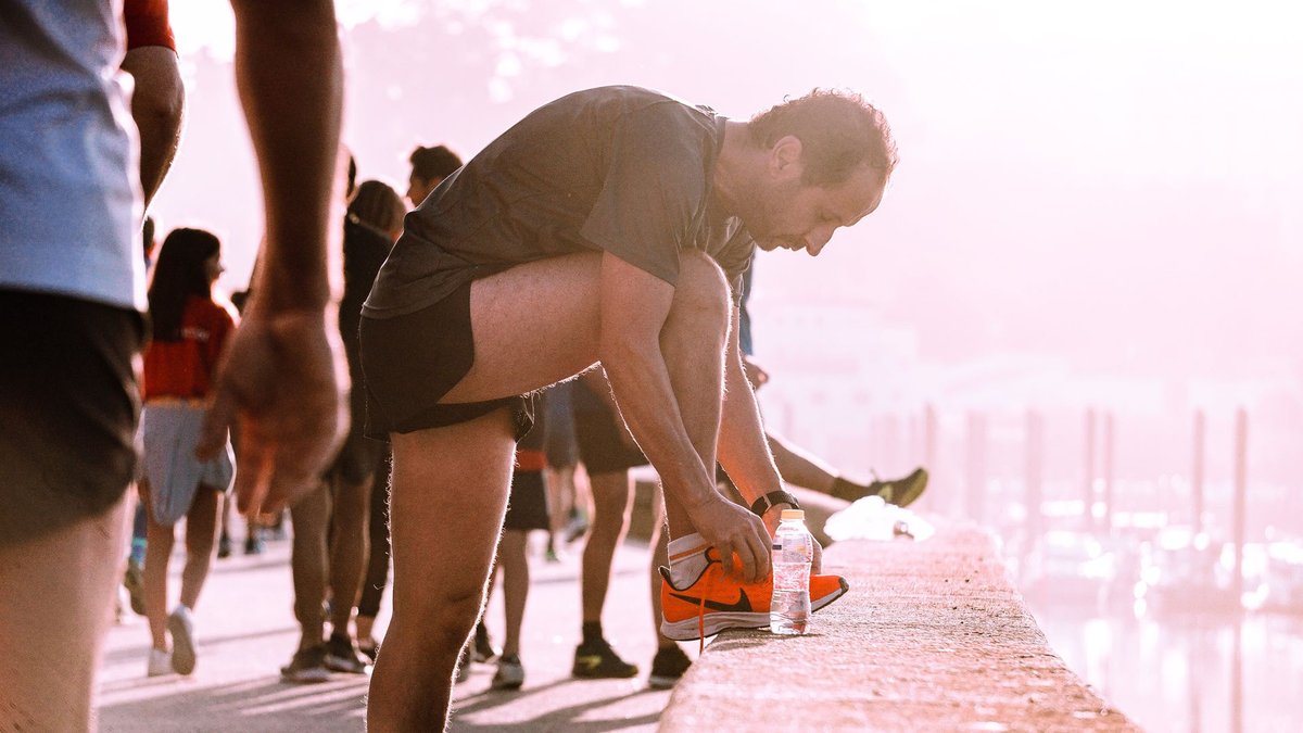 Corredor en un paseo marítimo al amanecer con una botella de agua: hacer ejercicio con calor