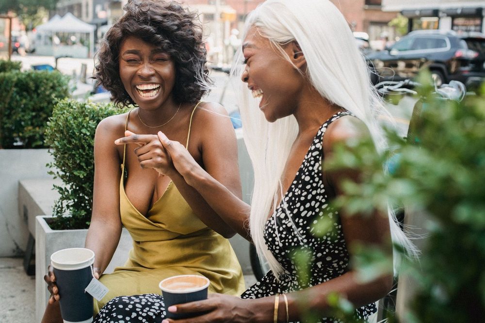 Zwei Freundinnen lachen beim Kaffee im Straßencafé – Einsamkeit überwinden und Energie durch echte Begegnung