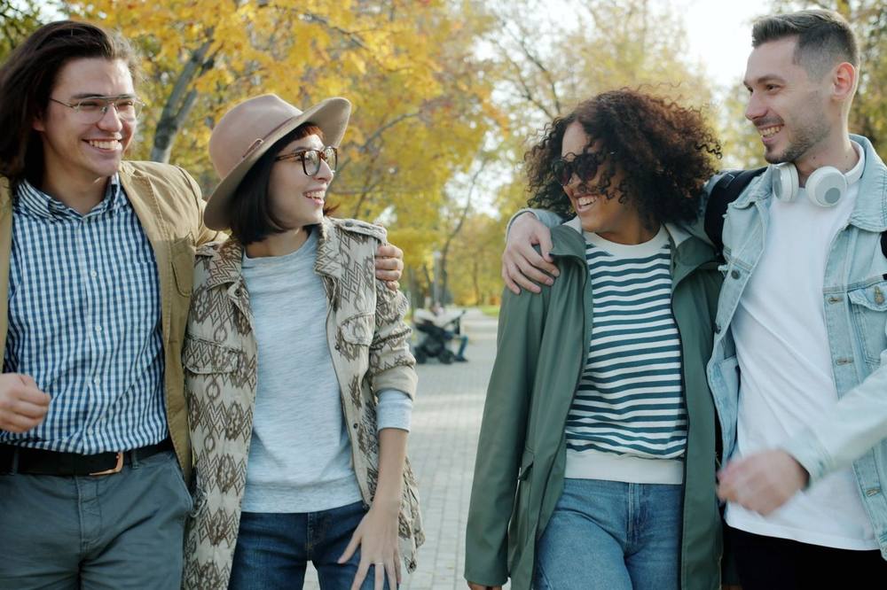 Amigos a rir durante um passeio num parque de outono cheio de sol — como aumentar a serotonina com luz, movimento e convívio