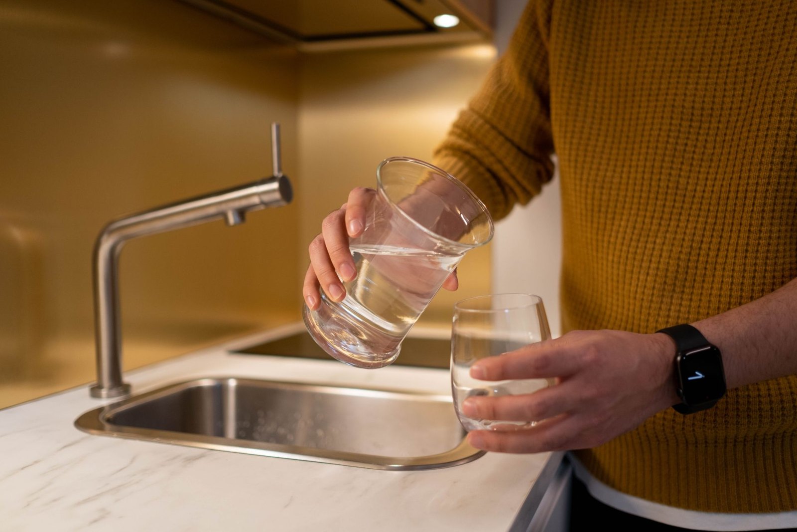 Seseorang menuang air di wastafel dapur — mengganti filter air