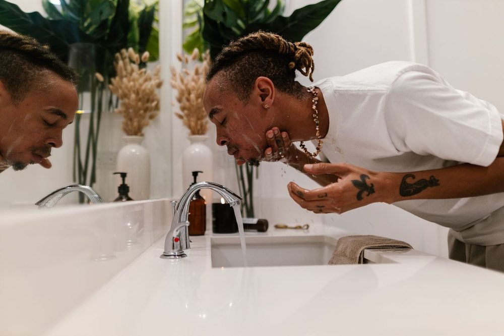 Hombre se lava la cara en el lavabo de un baño luminoso: cuidado facial sencillo para hombre
