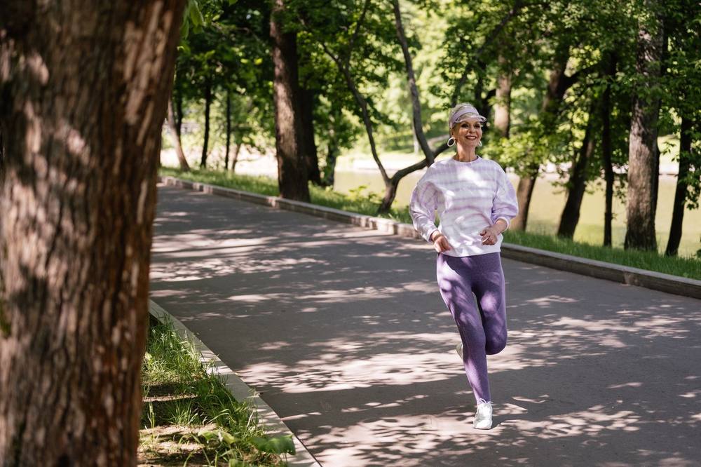 日差しの差す公園の小道を走る50代の女性。ミトコンドリアを増やす運動と細胞のエネルギー