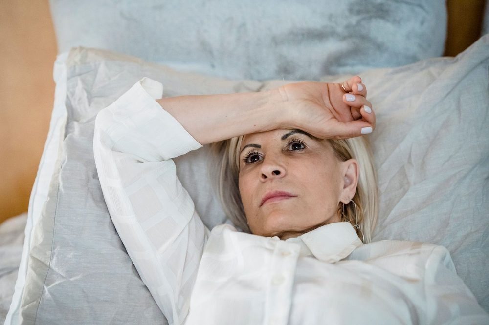 ผู้หญิงวัย 40 กว่านอนบนเตียงเอามือแตะหน้าผาก — perimenopause กับการนอนที่แปรปรวน