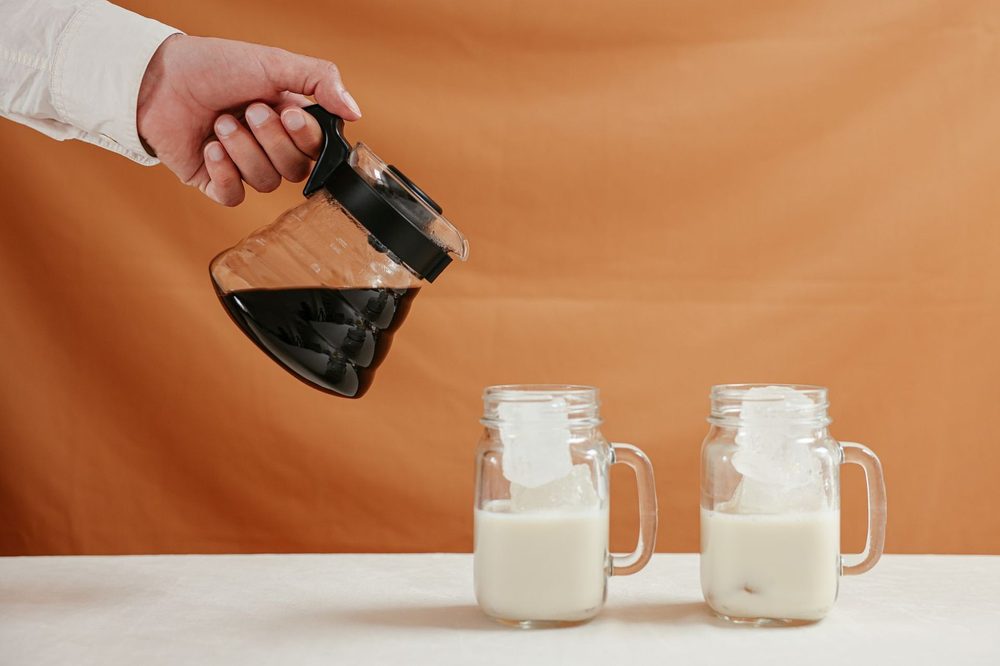 Café de uma cafeteira a ser servido em canecas de vidro com leite e gelo — café com proteína ao pequeno-almoço