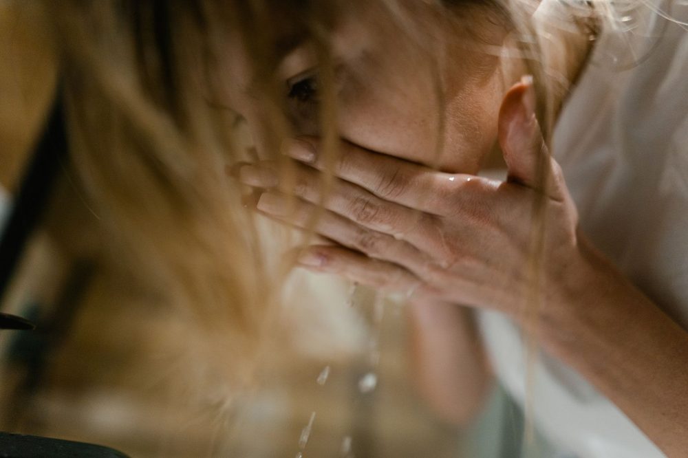 Une jeune femme se passe de l'eau fraîche sur le visage au lavabo le matin — visage gonflé le matin et rituel express