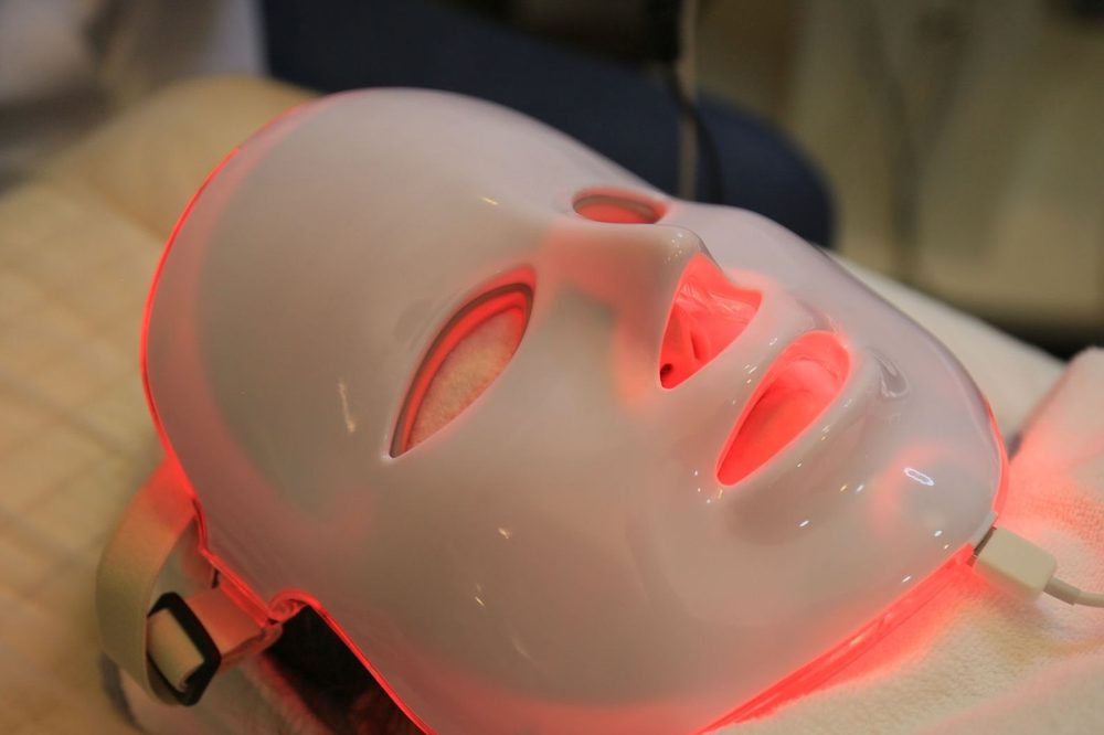 Masker LED bercahaya merah di wajah saat perawatan — manfaat red light untuk wajah